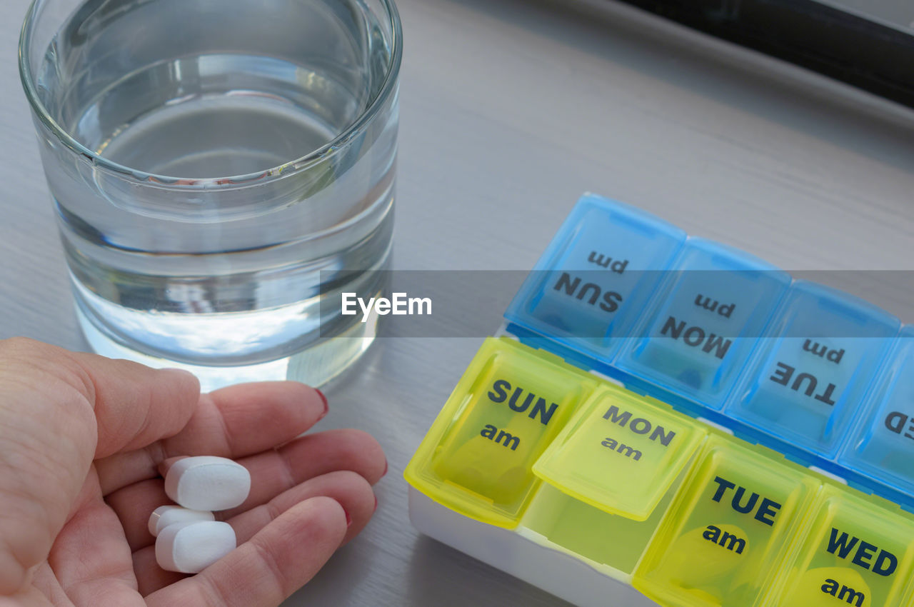 Close-up of woman hand holding pills by box and glass of water