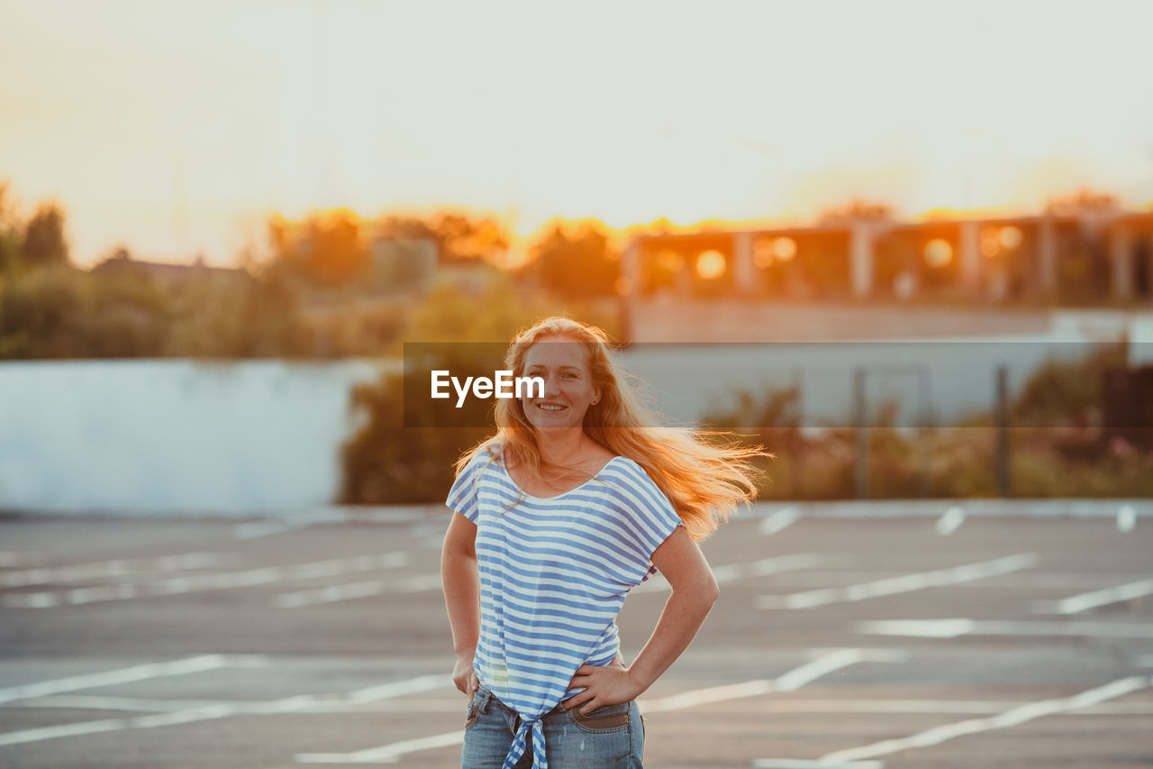 Portrait of smiling young woman standing against sky during sunset