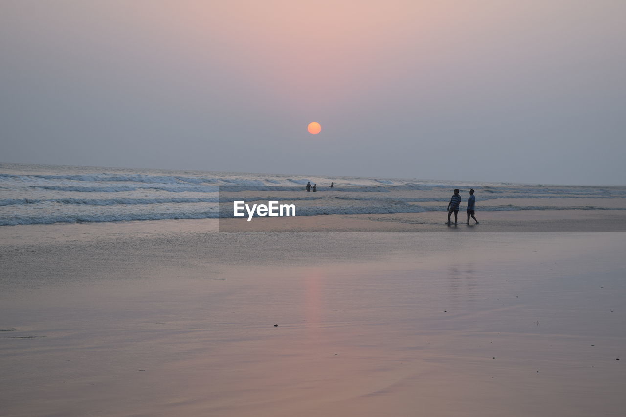 People walking on beach against sky during sunset