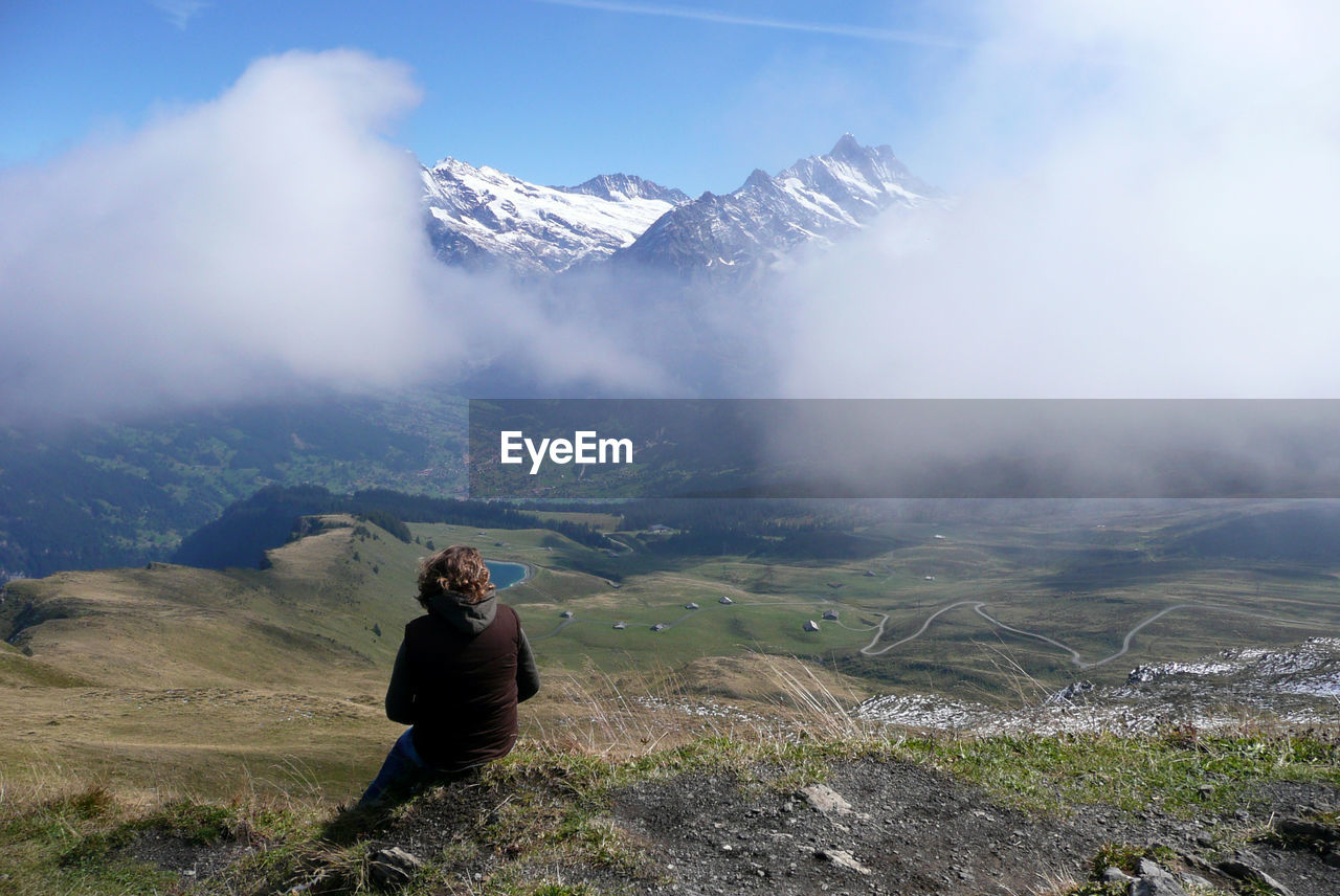 Rear view of woman sitting on mountain against sky