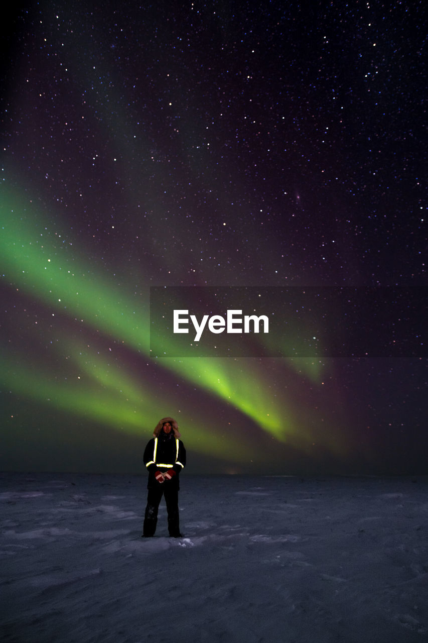 Full length of man standing on snow covered landscape against aurora borealis