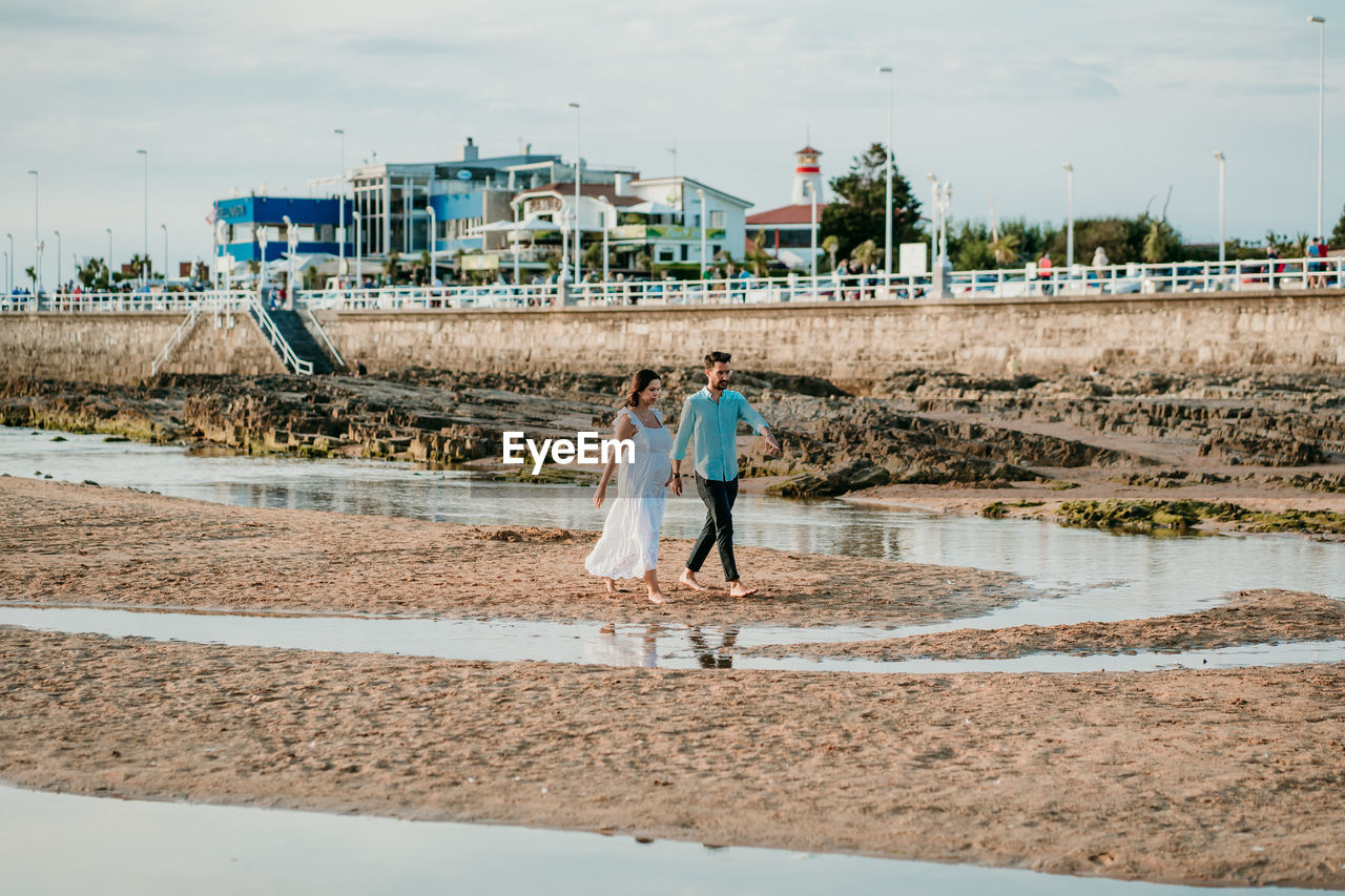 Full length of couple embracing while standing on beach against sky