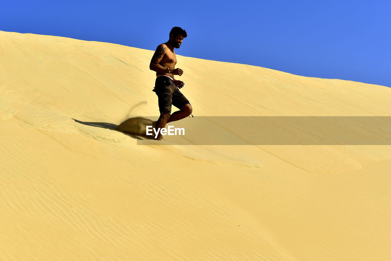 Man running on sand dune in desert against sky