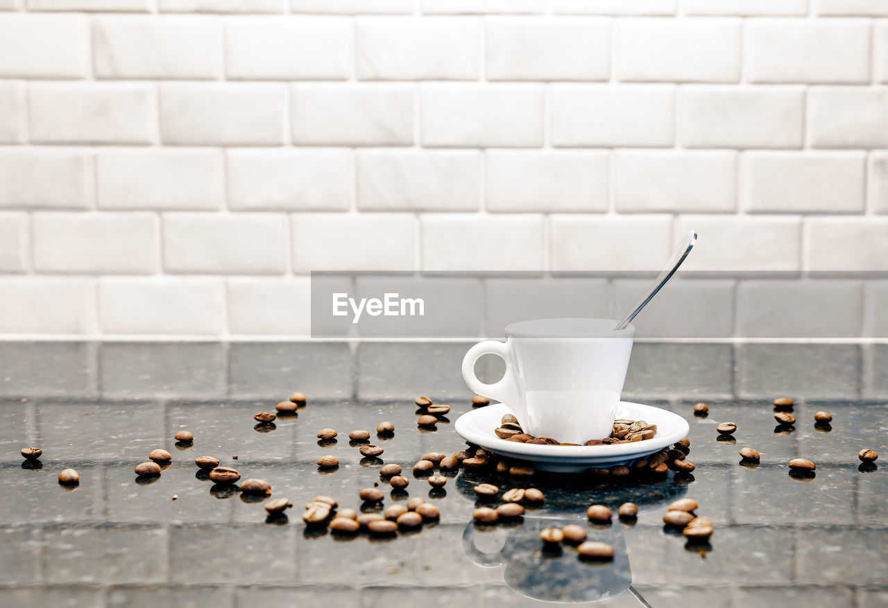 food and drink, coffee, mug, cup, coffee cup, drink, food, indoors, refreshment, wall, no people, hot drink, saucer, crockery, table, kitchen utensil, flooring, copy space, tableware, freshness, white, floor, brick wall, spoon, tile, studio shot, wall - building feature, still life, roasted coffee bean, coffee break