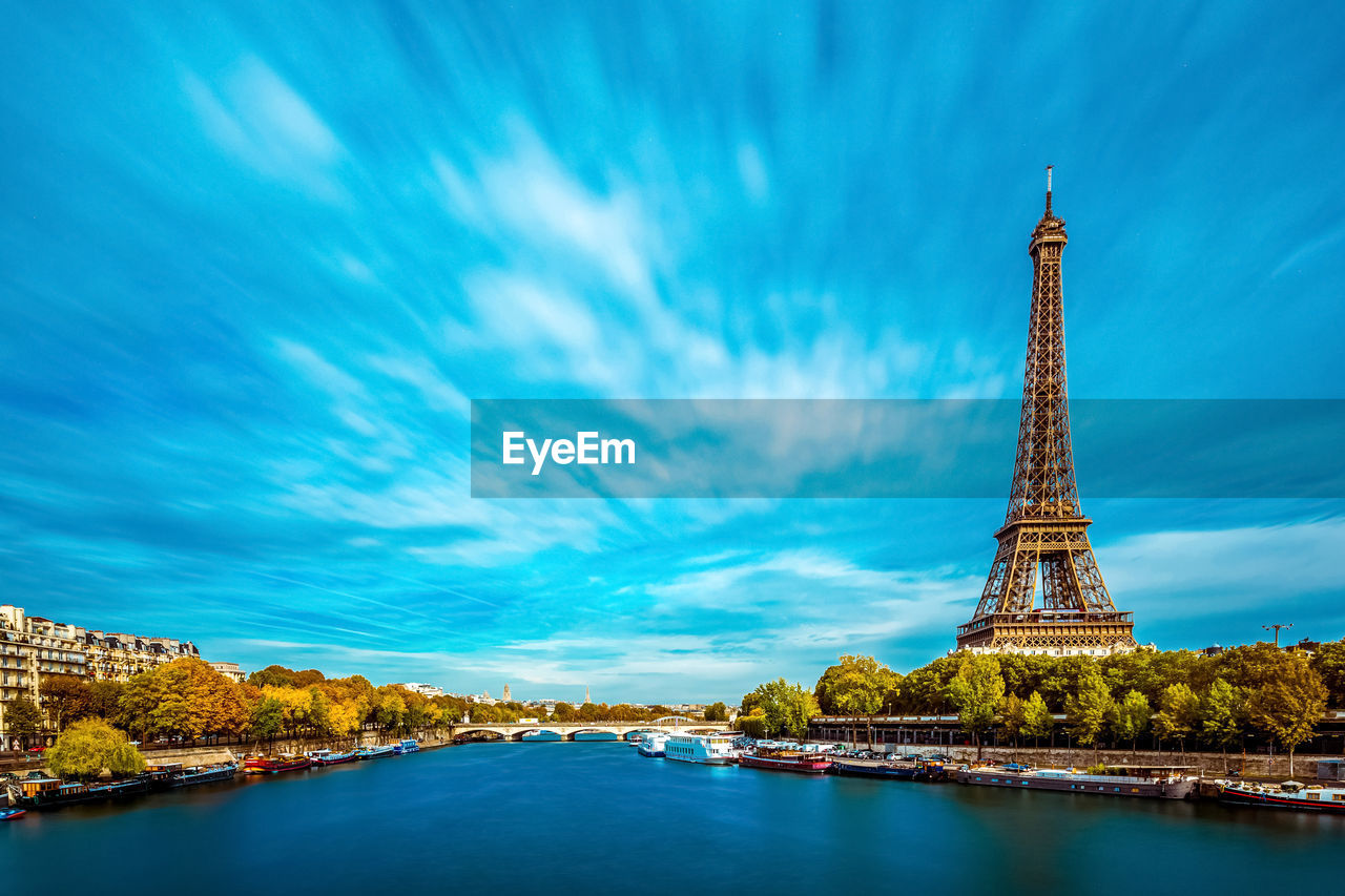 View of eiffel tower by river against cloudy sky