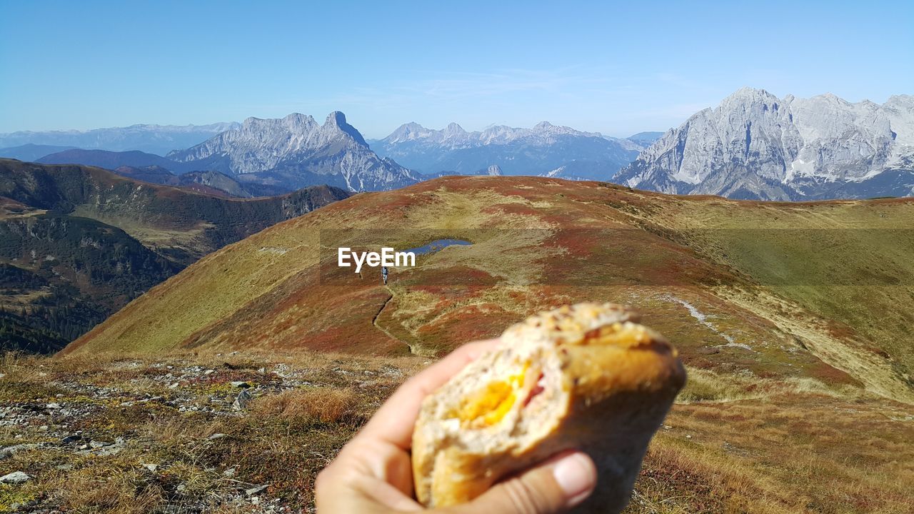 Cropped hand holding burger against mountain