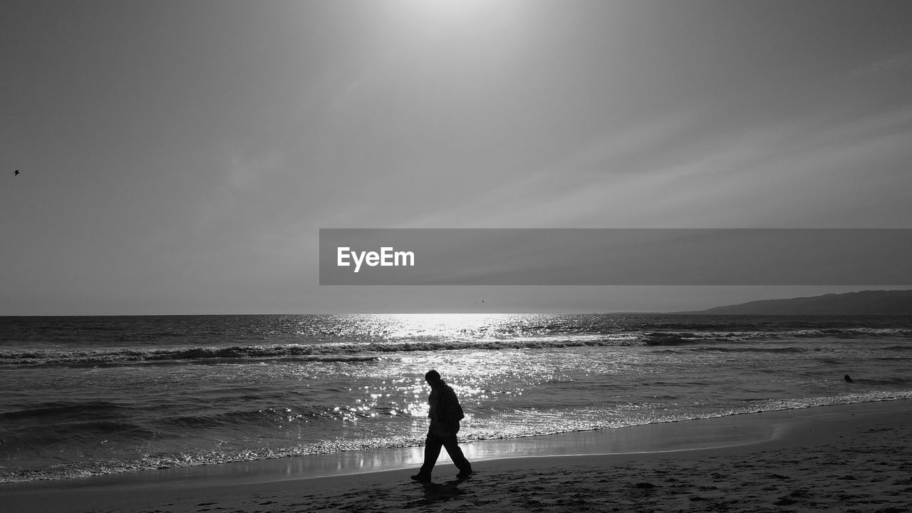 Silhouette man walking on beach against sky