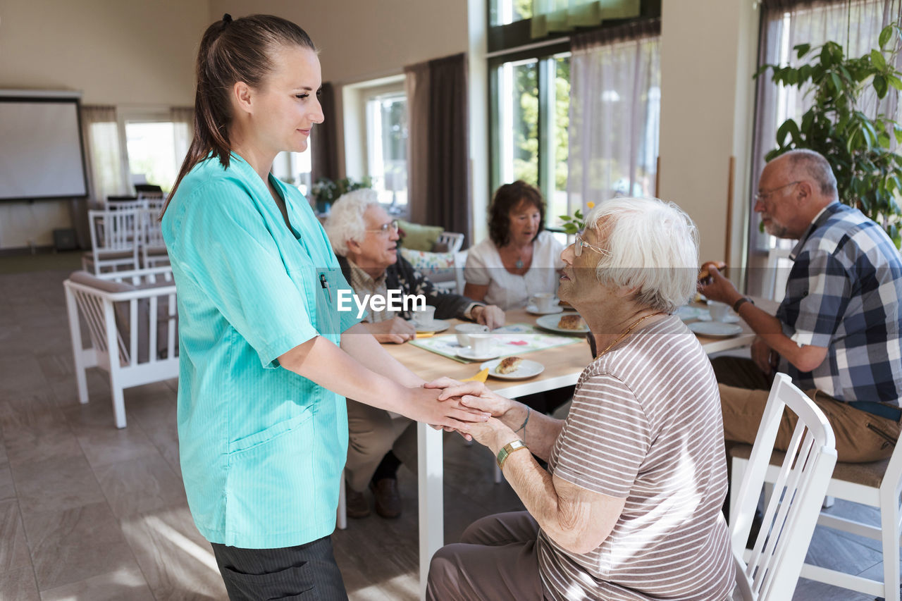 Nurse comforting senior woman while having breakfast at nursing home