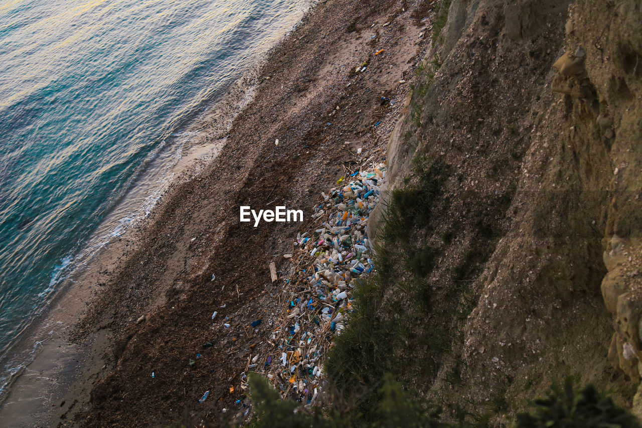 High angle view of garbage by cliff at beach during sunset