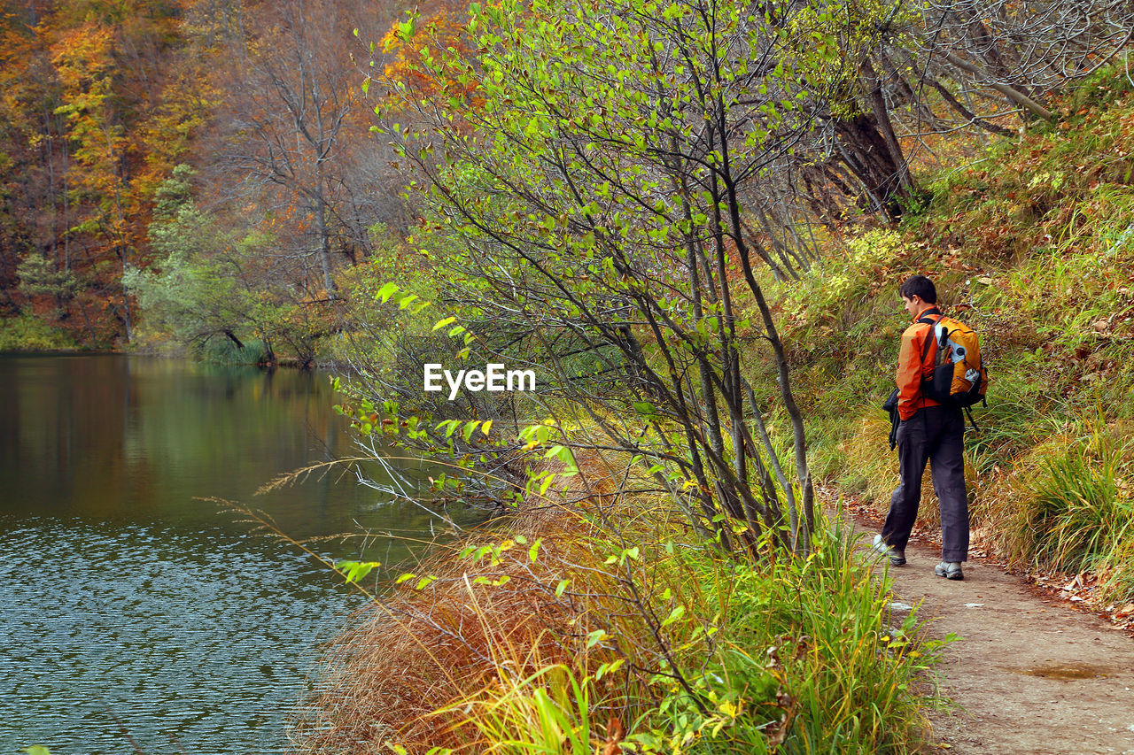 REAR VIEW OF MAN STANDING ON RIVERBANK