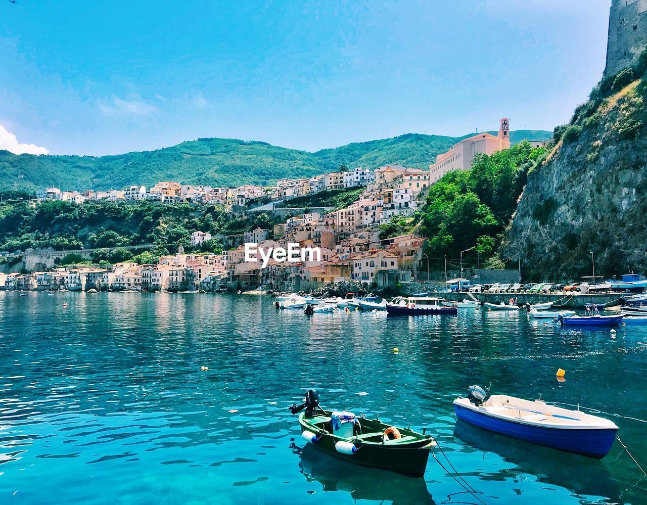 Sailboats moored in sea by townscape against sky