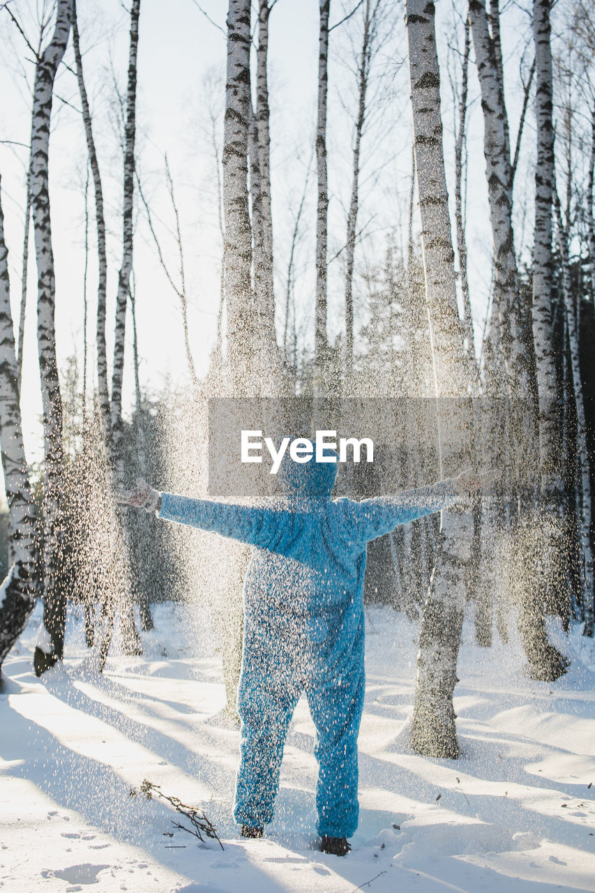 Rear view of mid adult man standing on snow covered field in forest