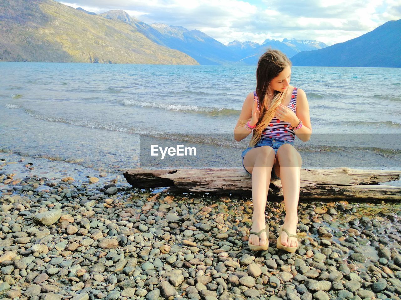 Full length of young woman sitting on pebbles at beach