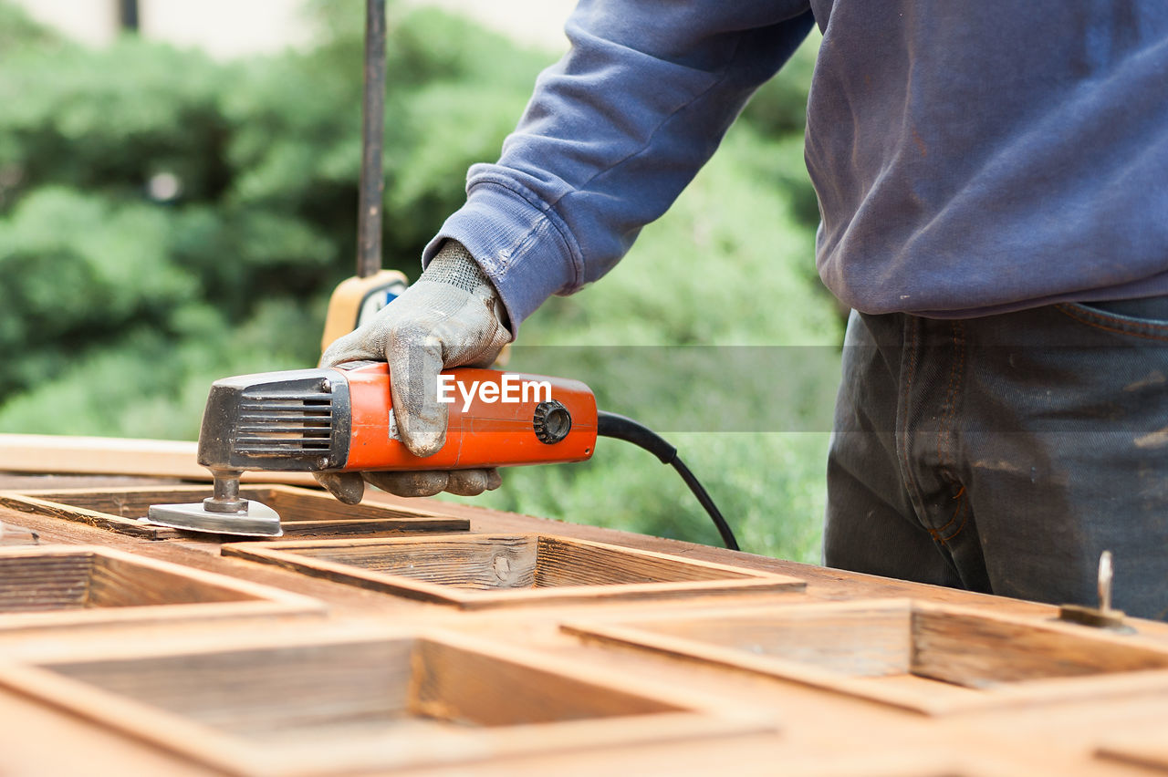 Close-up of man working with sander on wooden plank