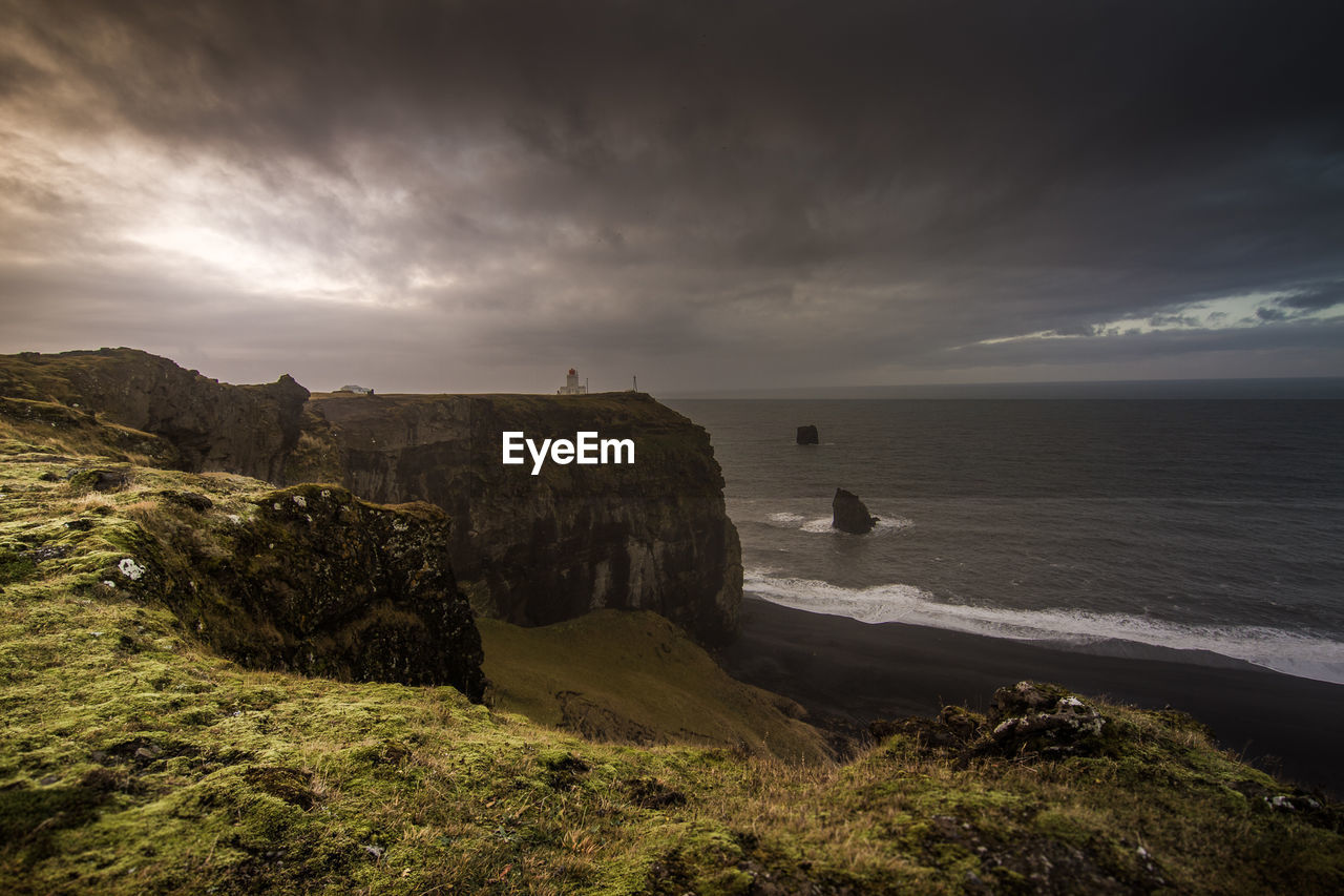 Scenic view of cliff by sea against cloudy sky