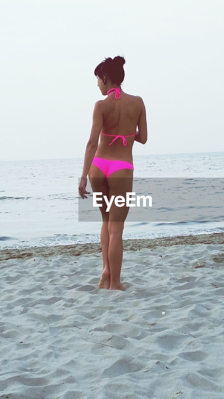 Rear view of woman in bikini standing at beach