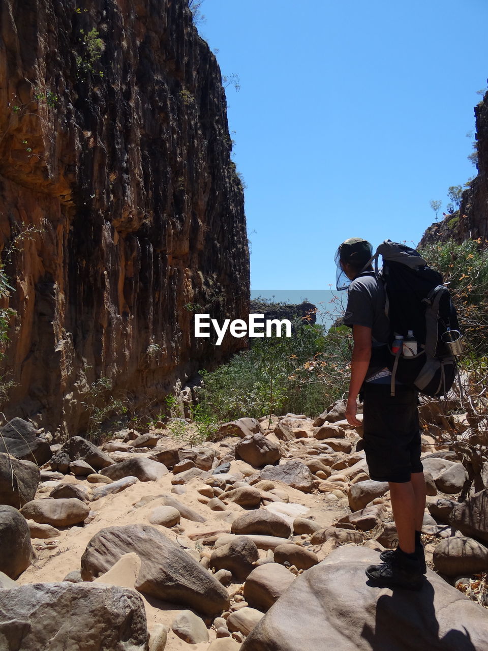 REAR VIEW OF MAN STANDING ON ROCKS AGAINST SKY