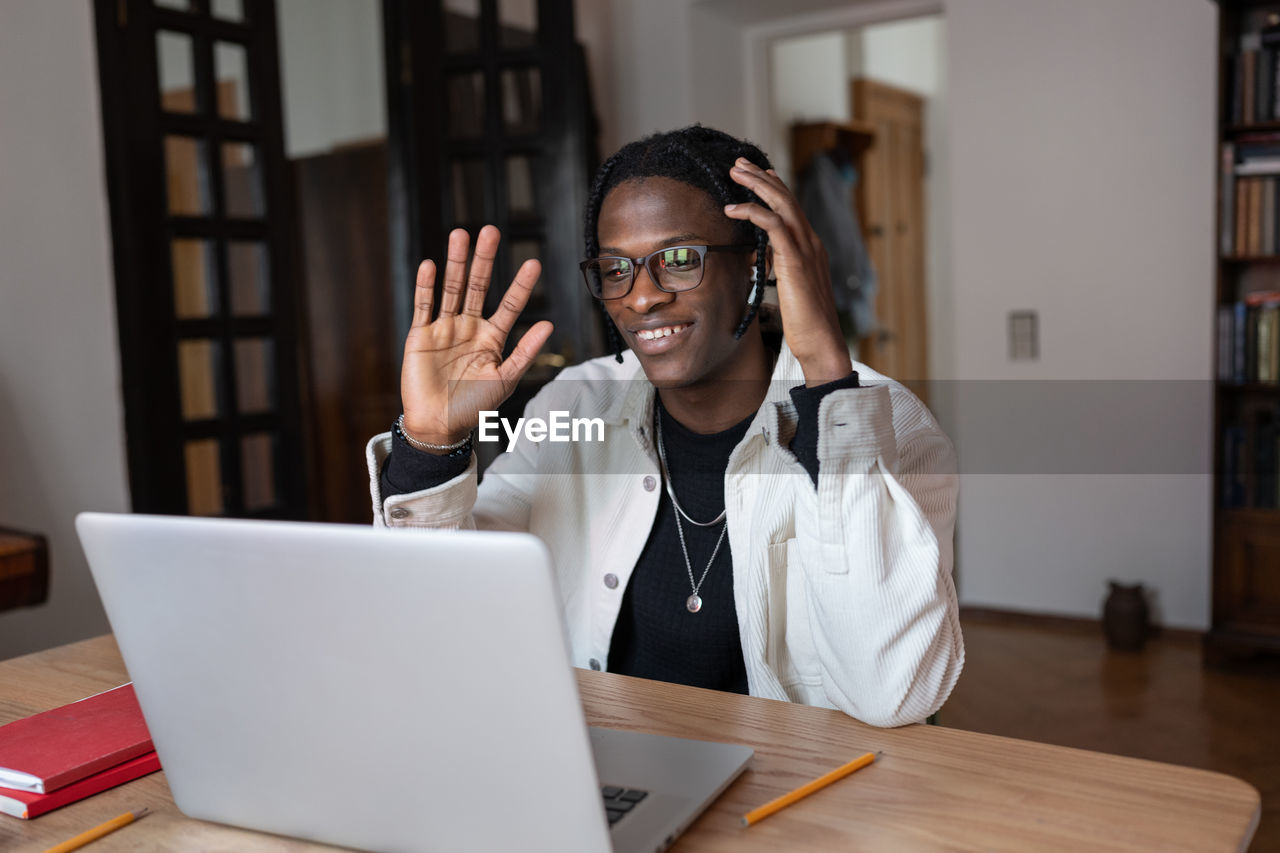 Smiling optimistic african american man waving hand having video call in laptop with friends