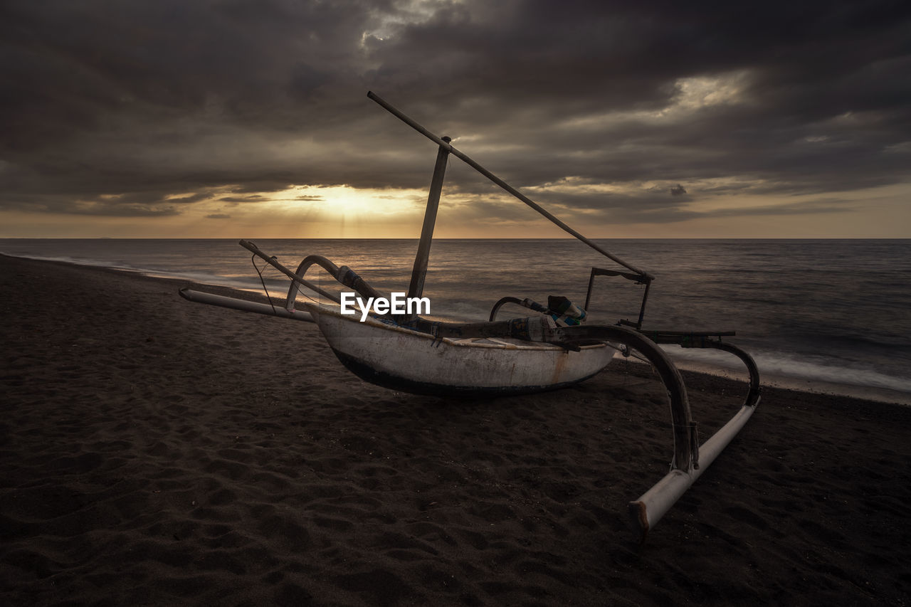 Fishing boat on beach against sky during sunset