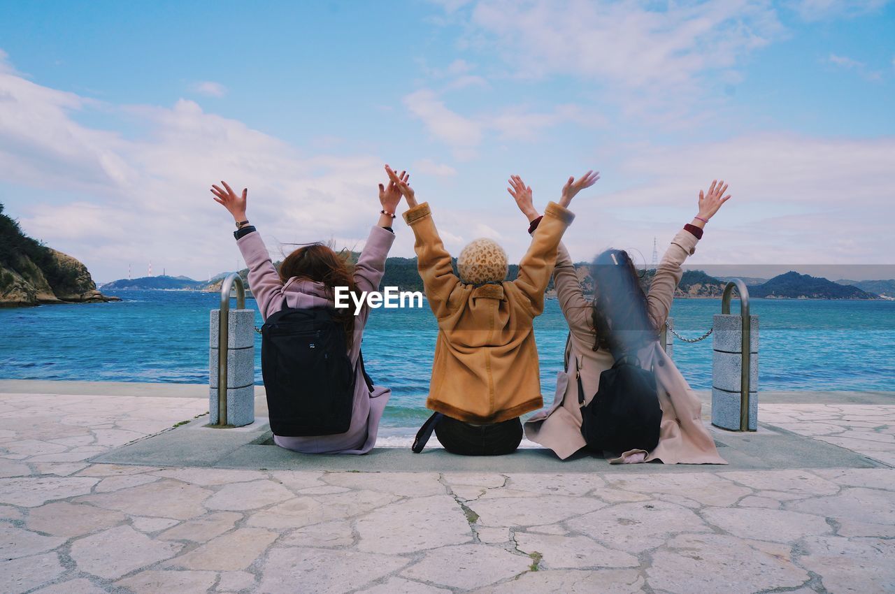 Rear view of friends sitting by sea against sky