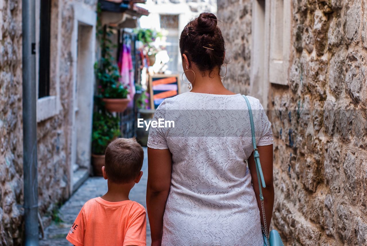 Rear view of mother and son walking in alley