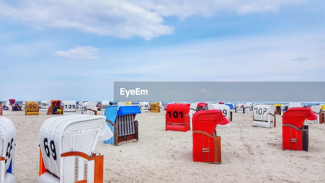 MULTI COLORED DECK CHAIRS ON SAND AT BEACH AGAINST SKY