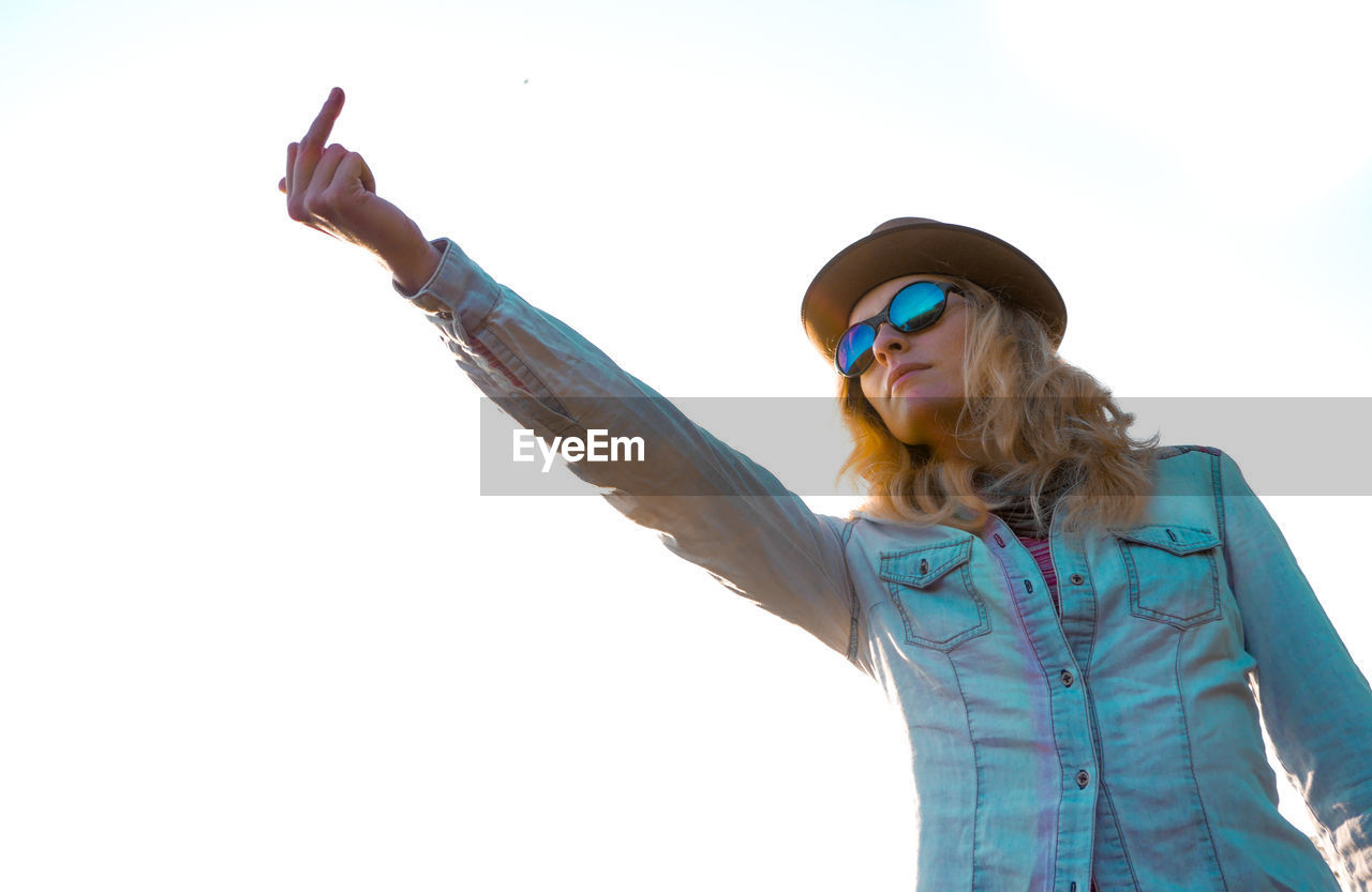 Woman in sunglasses showing obscene gesture against clear sky