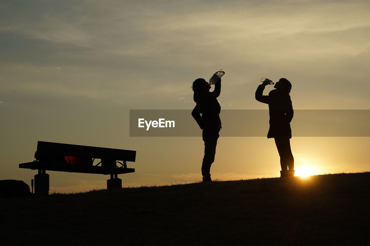 SILHOUETTE PEOPLE STANDING ON FIELD DURING SUNSET