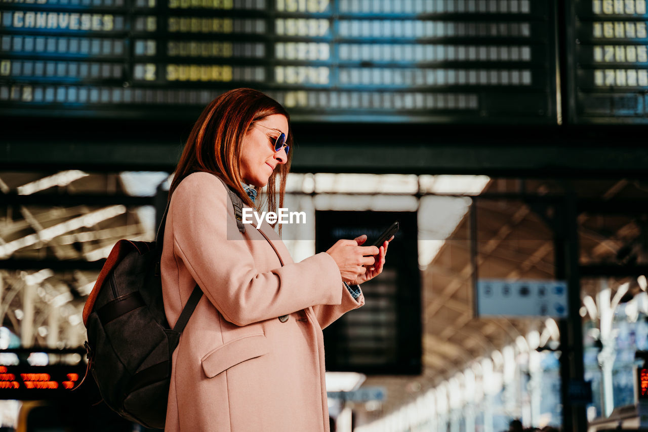 Woman using mobile phone while standing at railroad station