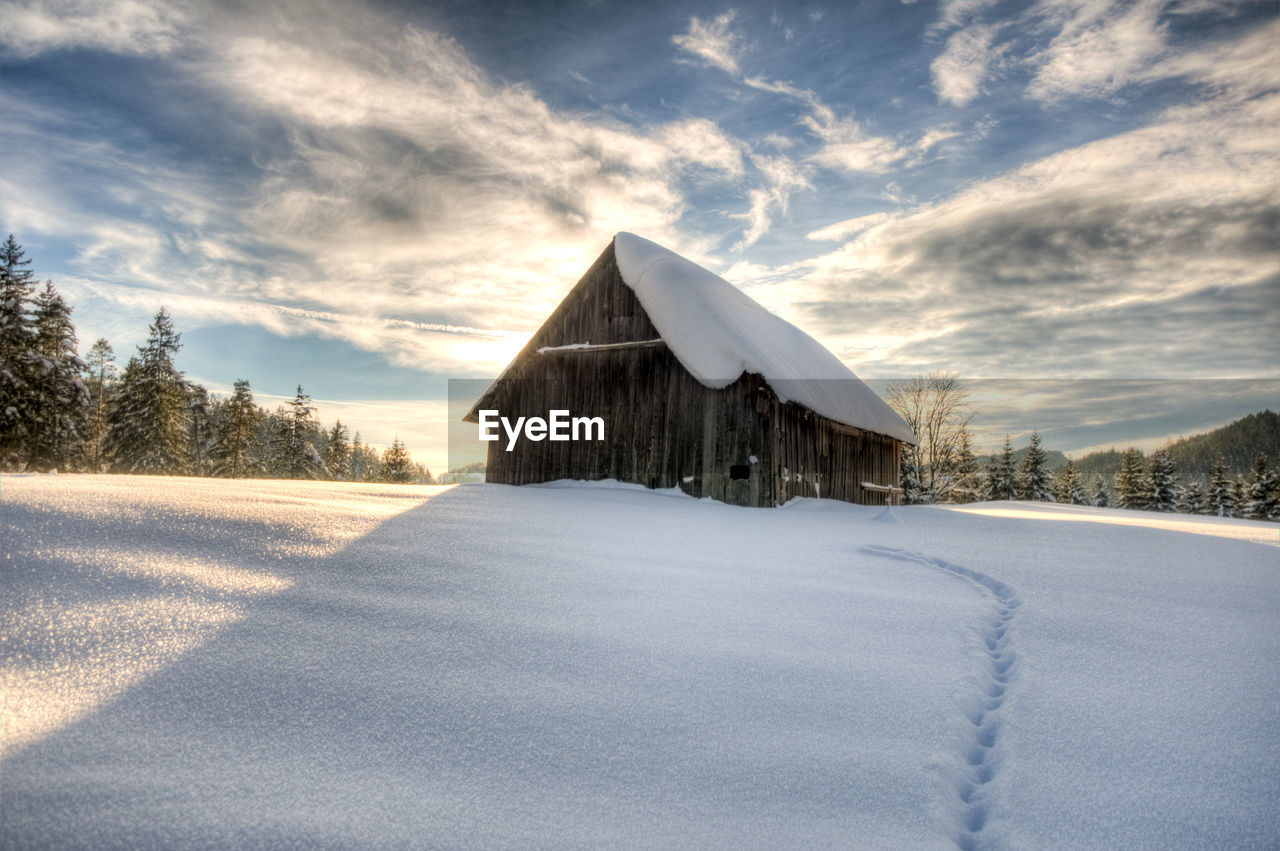 House on snowy field against sky during winter