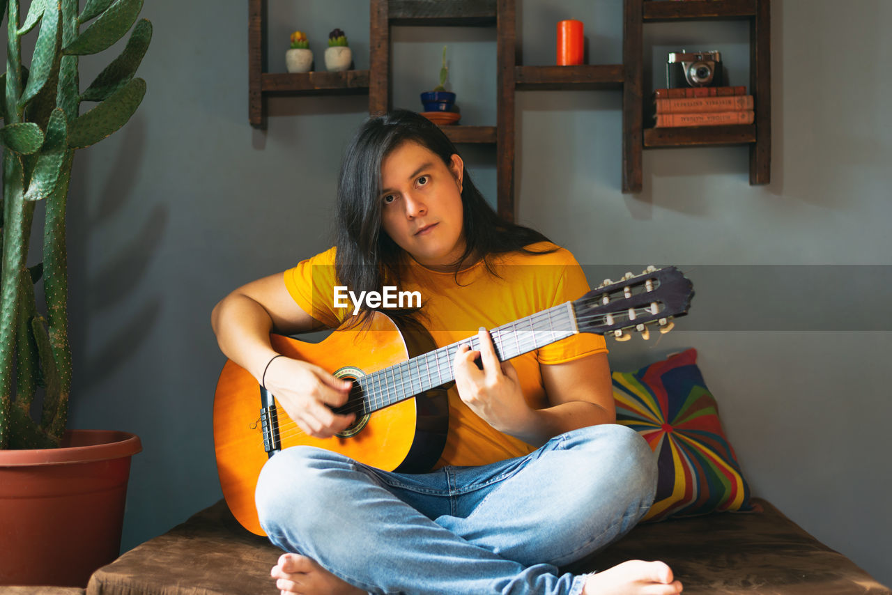 Man with long hair playing acoustic guitar at home during quarantine