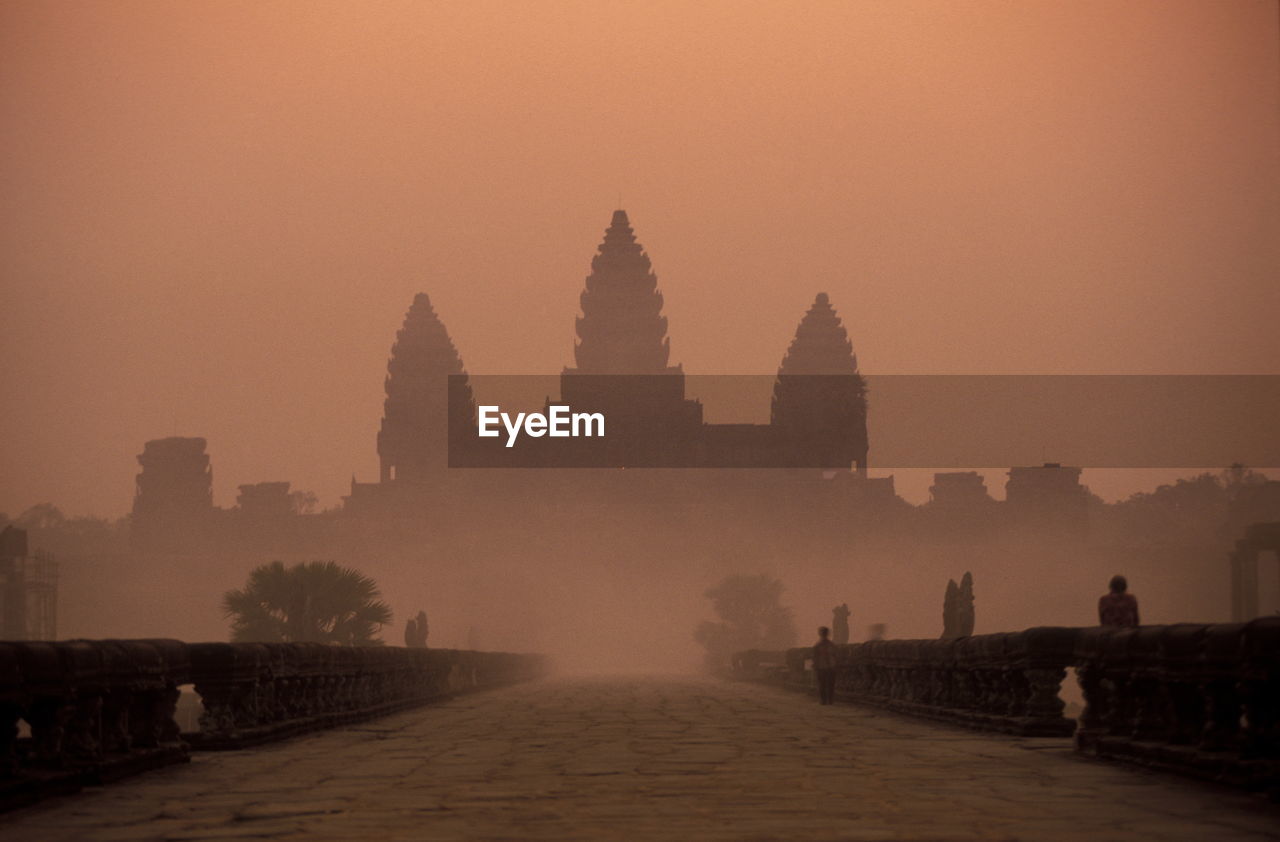 Pathway leading towards temple against sky during sunset