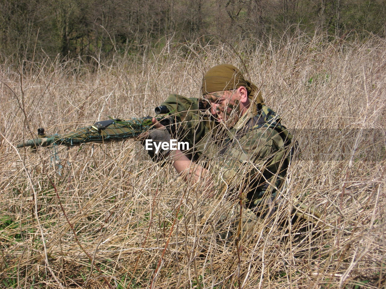 Sniped aiming with rifle at grassy field