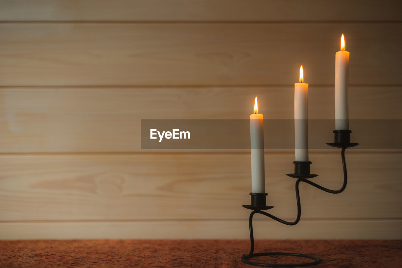 Burning candles glow in candlestick on desk surface. wooden background with copy space for text