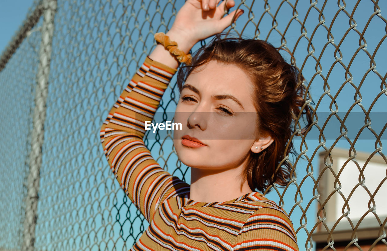 Portrait of young woman against fence