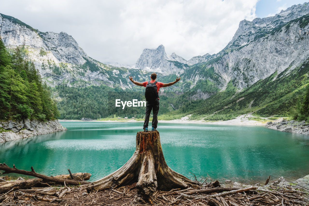 Happy traveler standing on tree stump admiring dachstein peak mountains on upper gosau lake, austria