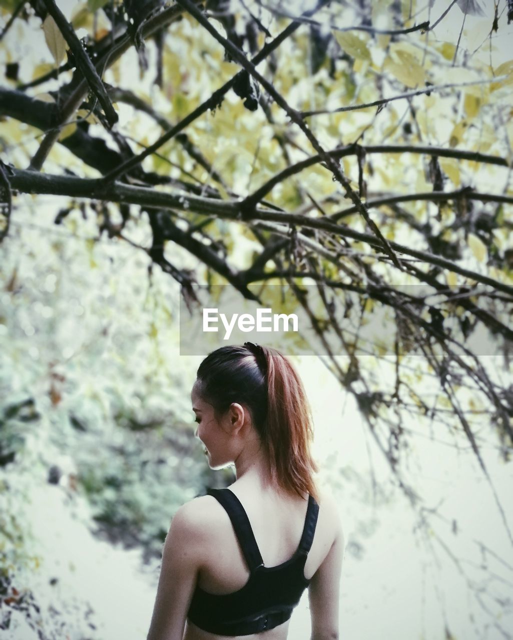 Rear view of young woman standing by tree