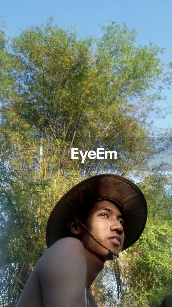 Low angle view of young man wearing hat against trees