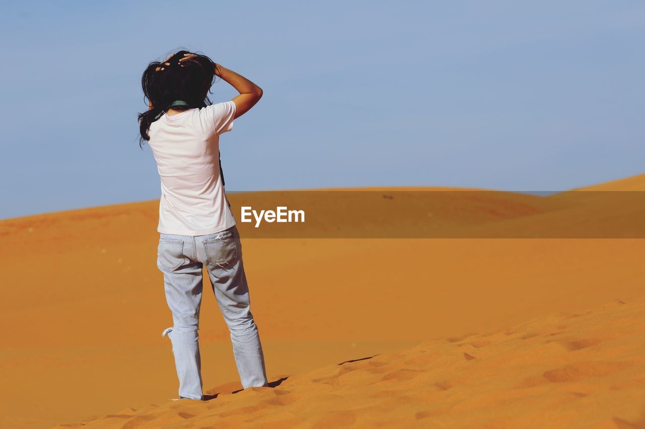 REAR VIEW OF MAN STANDING ON DESERT