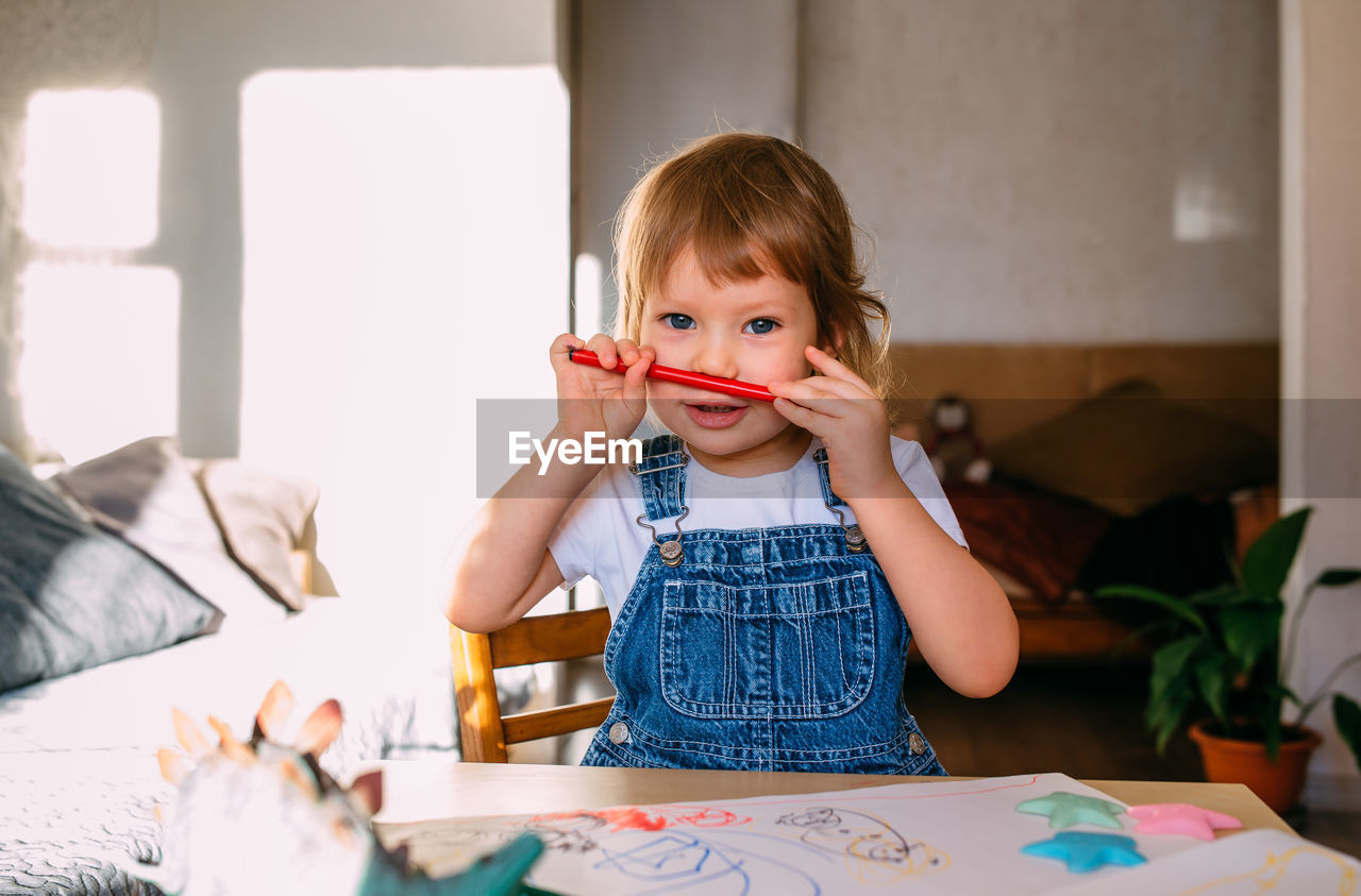 Small child at home at the children's table draws with felt-tip pens.