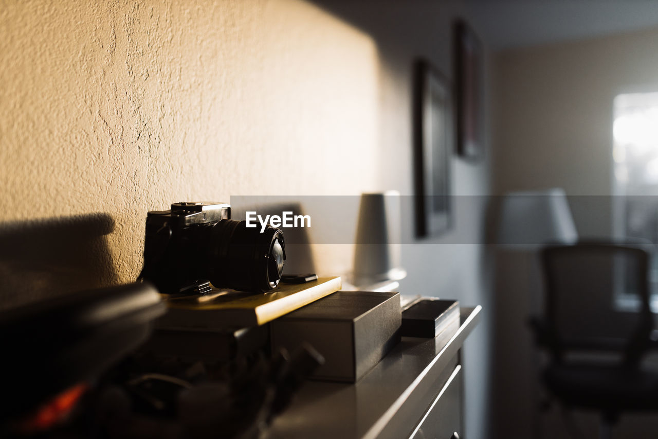 Professional photo camera illuminated by sunlight placed on wooden chest of drawers in room with contemporary interior