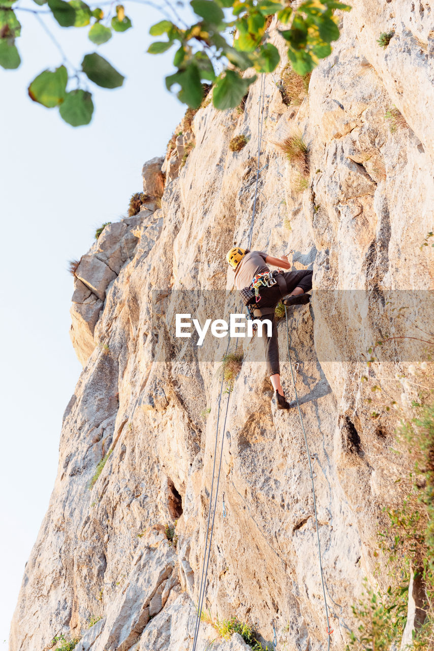 Sportive male alpinist climbing on sheer cliff in summer day