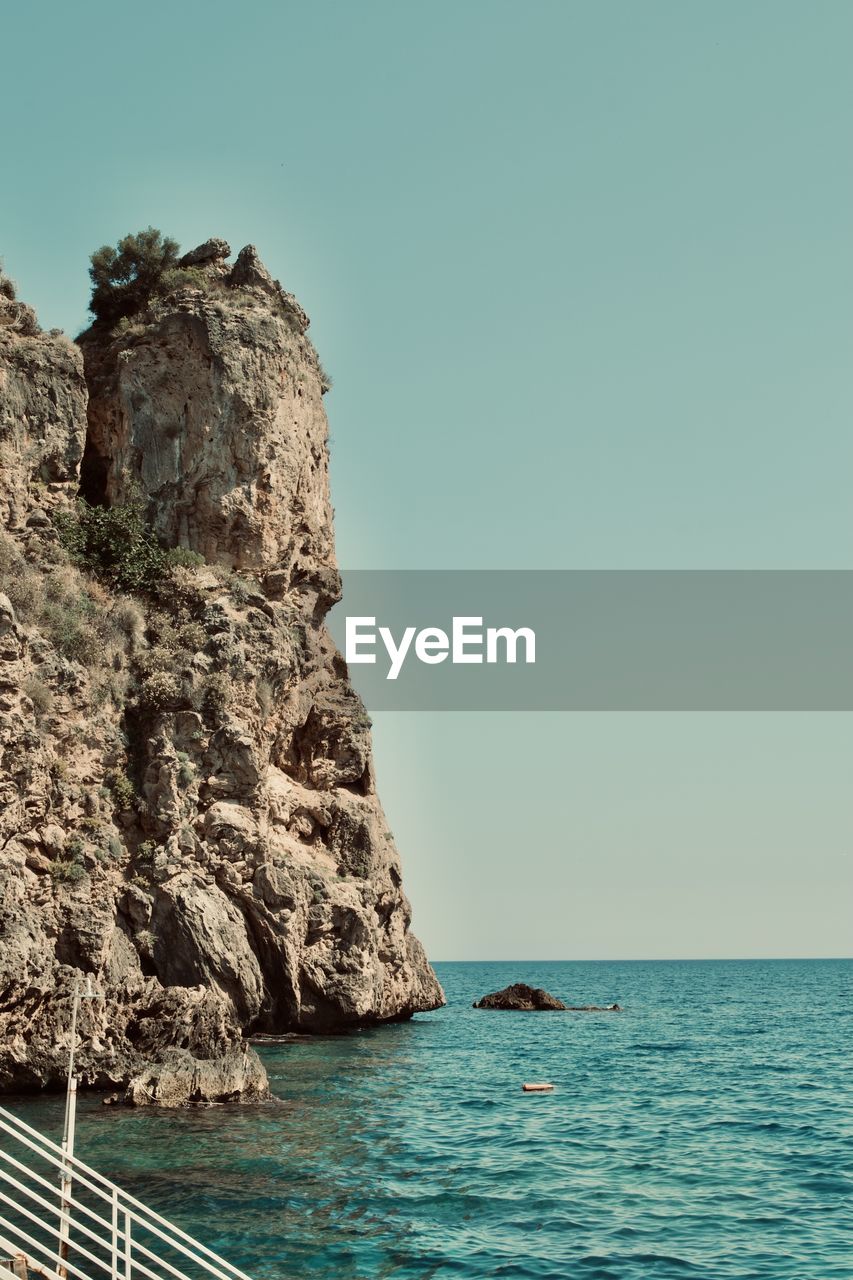 Rock formation in sea against clear sky