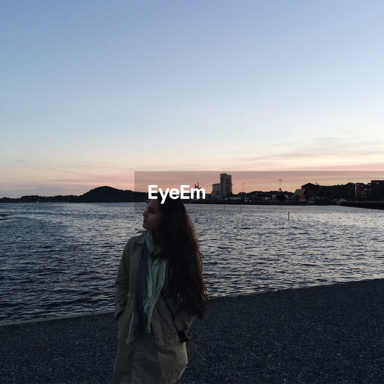 WOMAN STANDING ON CITY BY SEA AGAINST CLEAR SKY IN WINTER