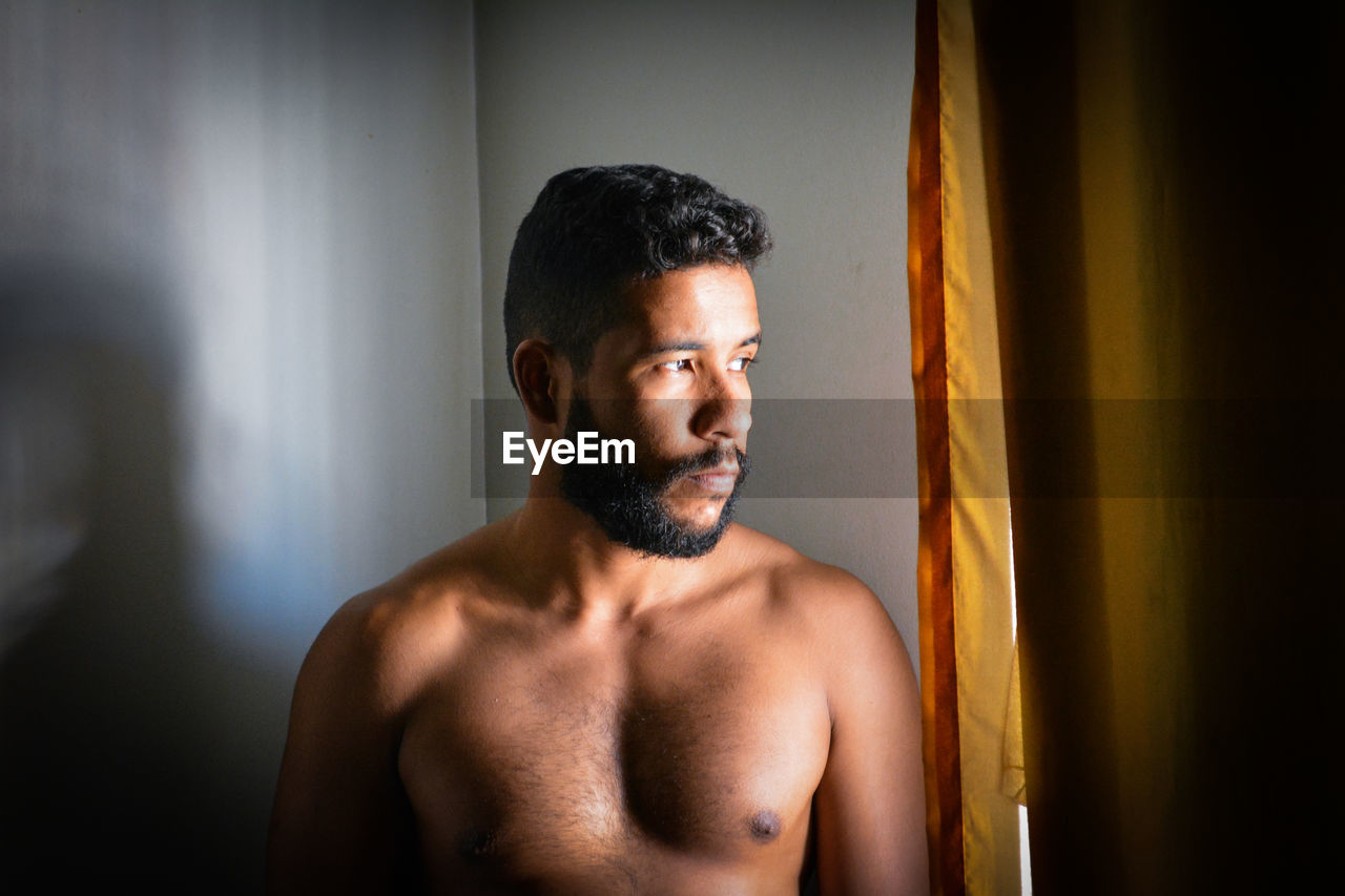 Shirtless man looking away at home