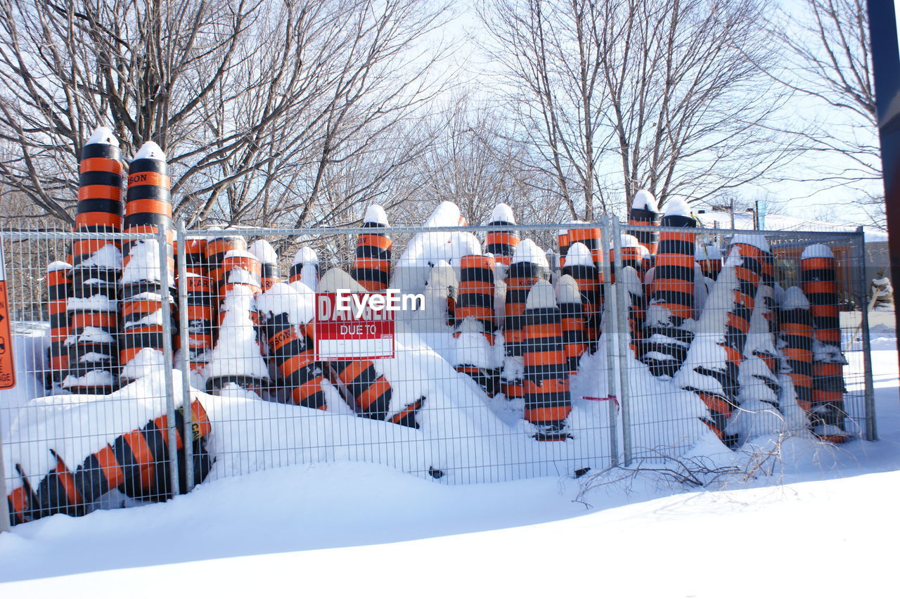 Snow covered traffic cones in fence with warning sign