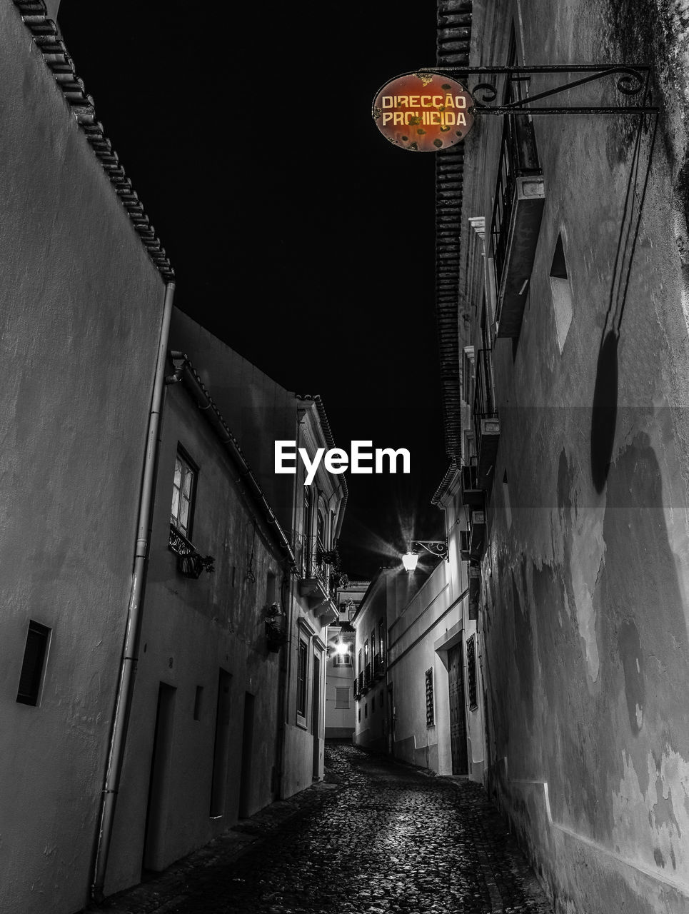 LOW ANGLE VIEW OF ILLUMINATED ALLEY AMIDST HOUSES AGAINST SKY