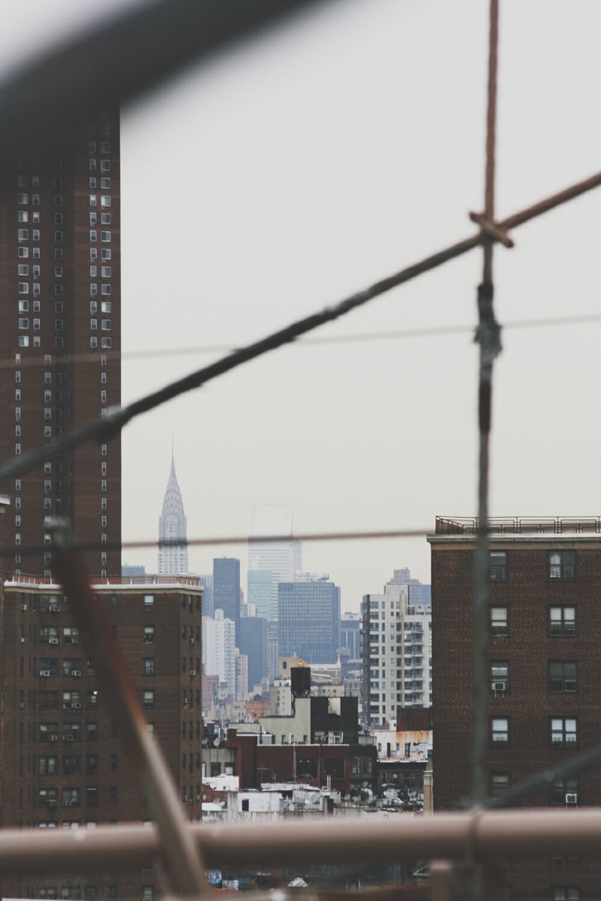 Chrysler building in city against sky seen through railing on sunny day