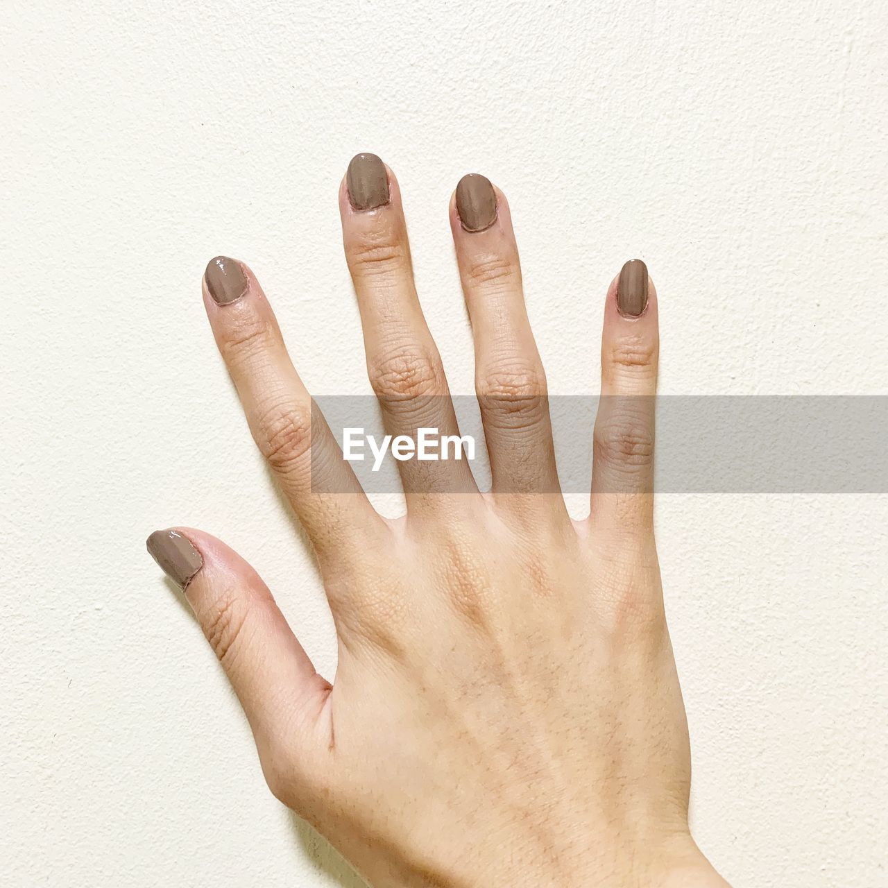 Cropped hand of woman with nail polish on white background