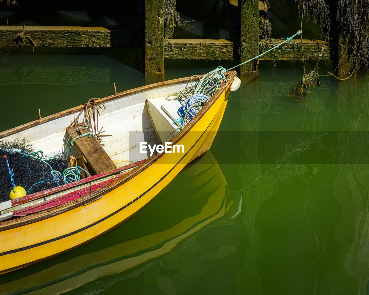 Yellow rowing boat moored up by rope and reflections in the water